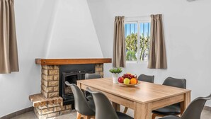 Een eetruimte met een houten tafel, zwarte stoelen, een stenen openhaard en een fruitschaal op de tafel.
