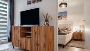 A modern living room with a wooden entertainment unit, a flat-screen TV, a sofa, and a dining area. - Apartment 'Fewo Seehase ' with Balcony and Wi-Fi (Wurster Nordseeküste)