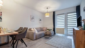 A modern living room with a sofa, dining table, chairs, a small side table, and a TV. - Apartment 'Fewo Seehase ' with Balcony and Wi-Fi (Wurster Nordseeküste)