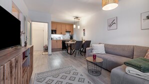 A modern living room with a flat-screen TV, a sofa, a coffee table, and a dining area with chairs and a table. - Apartment 'Fewo Seehase ' with Balcony and Wi-Fi (Wurster Nordseeküste)