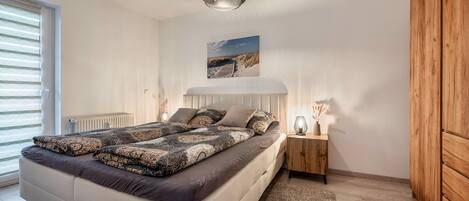 Un dormitorio con cama, lámparas de noche, un cuadro en la pared y una ventana.