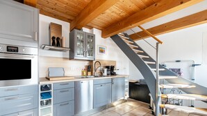 Une cuisine moderne dotée d’appareils électroménagers en acier inoxydable, d’un plafond en bois et d’un escalier.