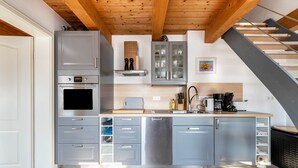 Une cuisine moderne avec des meubles gris, un four encastré, un lave-vaisselle en acier inoxydable et un plafond en bois.