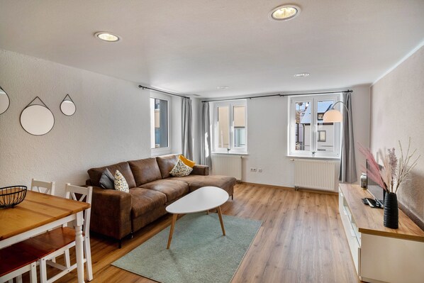 A modern living room with a brown sofa, white coffee table, and a dining area with a wooden table and chairs.