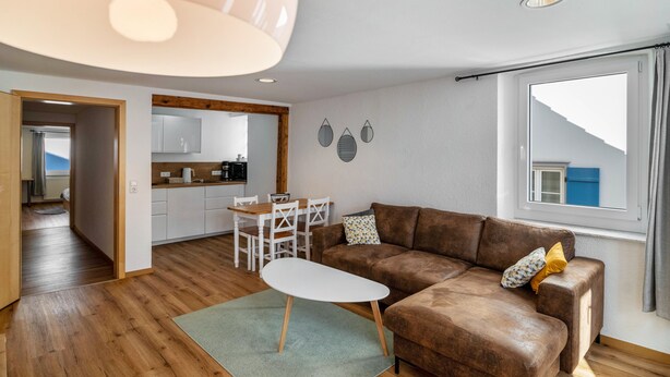 Ein modernes Wohnzimmer mit einem braunen Sofa, einem weißen Couchtisch und einem Essbereich mit einem Holztisch und Stühlen.