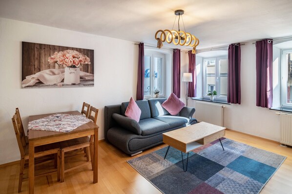 A living room with a sofa, a wooden dining table, a coffee table, and a painting on the wall.