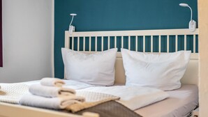 Cama com roupa de cama branca, cabeceira branca e parede verde-água.