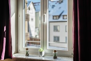 A window with a view of buildings, a potted plant, and a small jar with seeds.