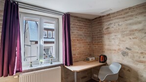 A corner room with a window, radiator, desk, chair, and a brick wall. - Single Room 57 with Wi-Fi (Bad Waldsee)