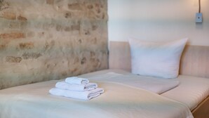 A neatly made bed with folded towels, a plain wall, and a wall-mounted light fixture. - Single Room 57 with Wi-Fi (Bad Waldsee)