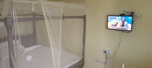 A room with a bed under a mosquito net, a television on the wall, and a power outlet. - Hillview Heights Haven Guest & Hotel (Webuye)