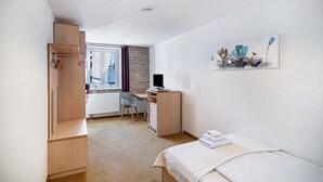 A hotel room with a bed, a desk, a chair, a radiator, and a window with curtains. - Single Room 52 with Wi-Fi (Bad Waldsee)