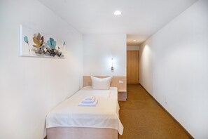 A hotel room with a bed, a nightstand, a painting on the wall, and a hallway leading to another room.