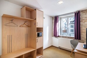 A room with a wooden wardrobe, a desk, a chair, a radiator, and a window with curtains.