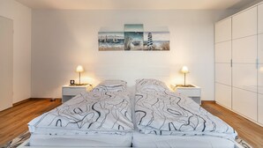 Ein Schlafzimmer mit einem Bett, zwei Nachttischen mit Lampen, einem Wandbild und einem Kleiderschrank.