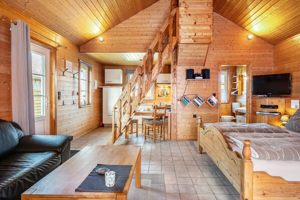 L’intérieur d’un chalet en bois comprend un escalier, un canapé, un lit, un coin repas et un téléviseur.