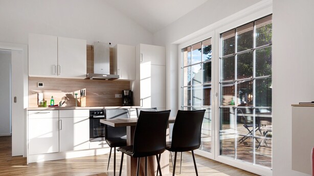 Una cocina moderna con armarios blancos, encimera de madera y un comedor con sillas negras.