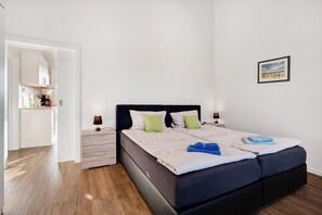 Un dormitorio con cama, mesitas de noche, lámpara, un cuadro en la pared y vistas a la cocina contigua.