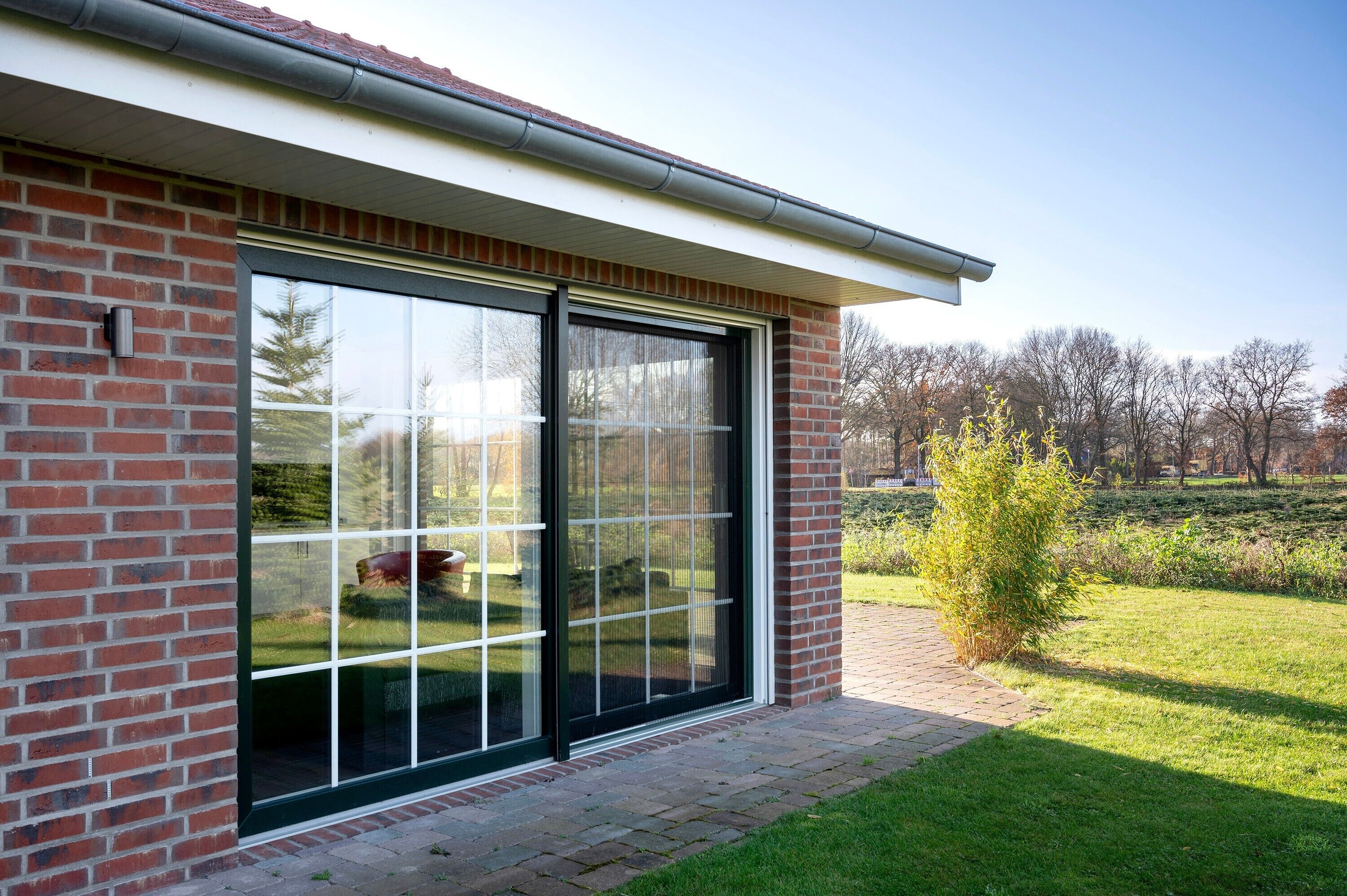 Ein modernes Gebäude mit großen Glasschiebetüren, einer Ziegel-Fassade und einem Rasenstück mit Bäumen.