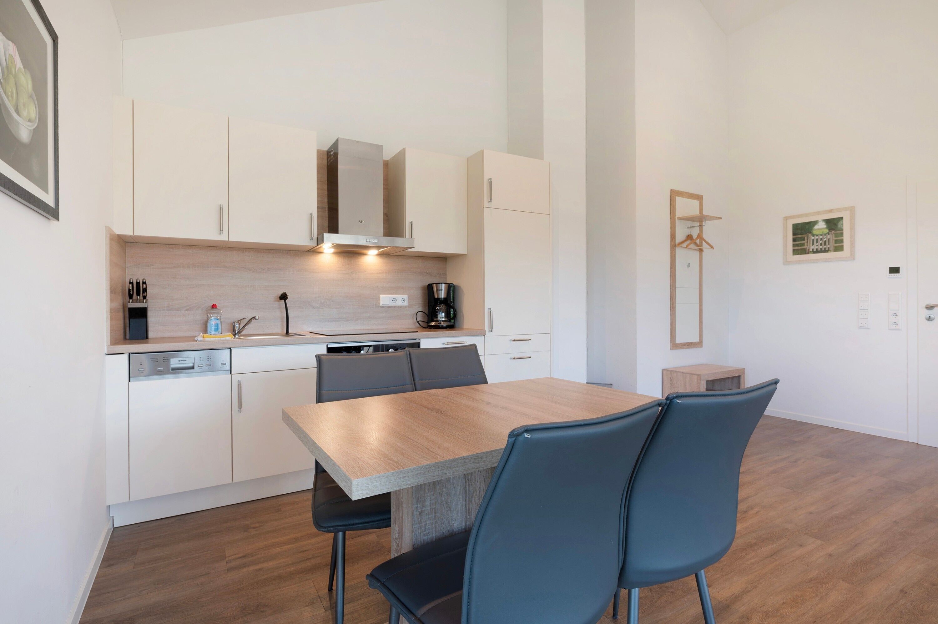 Een moderne keuken met witte kasten, een houten eettafel en blauwe stoelen.
