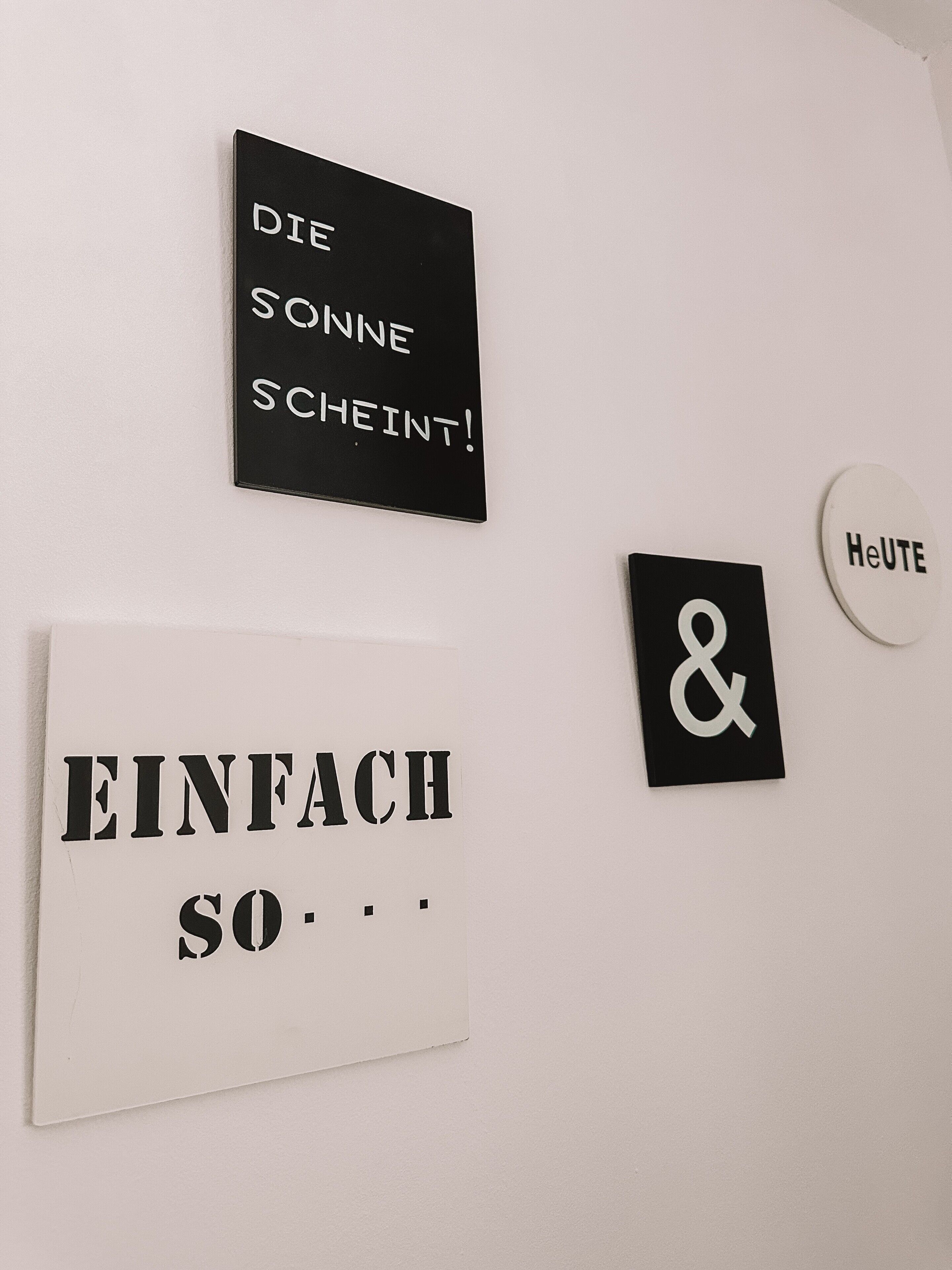 Three signs on a wall: 'DIE SONNE SCEINT!', 'EINFACH SO...', and '&'.