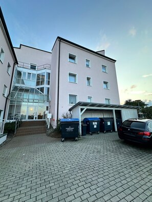 Un bâtiment avec une entrée en verre, un espace de stationnement couvert et une BMW garée devant.