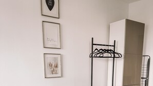 Ein modernes Wohnzimmer mit einer Couch, einem kleinen Beistelltisch, einem Topf mit Pflanze, einem Kleiderständer und einem Kleiderschrank.
