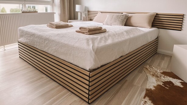 Ein modernes Schlafzimmer mit einem großen Bett, einem Holz-Kopfteil und Blick auf die Stadt.
