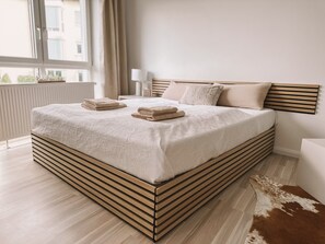 Une chambre moderne avec un grand lit, une tête de lit en bois et une vue sur la ville.