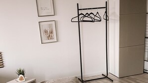 Ein Schlafzimmer mit Bett, Kleiderstange, Kleiderschrank und gerahmten Bildern an der Wand.