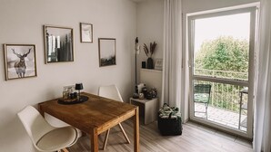 Ein modernes Wohnzimmer mit einem Holzesstisch, weißen Stühlen und einem großen Fenster mit Blick ins Grüne.