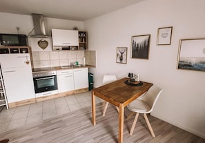 Una cocina con armarios blancos, una mesa de comedor de madera y sillas. Hay cuadros en la pared.