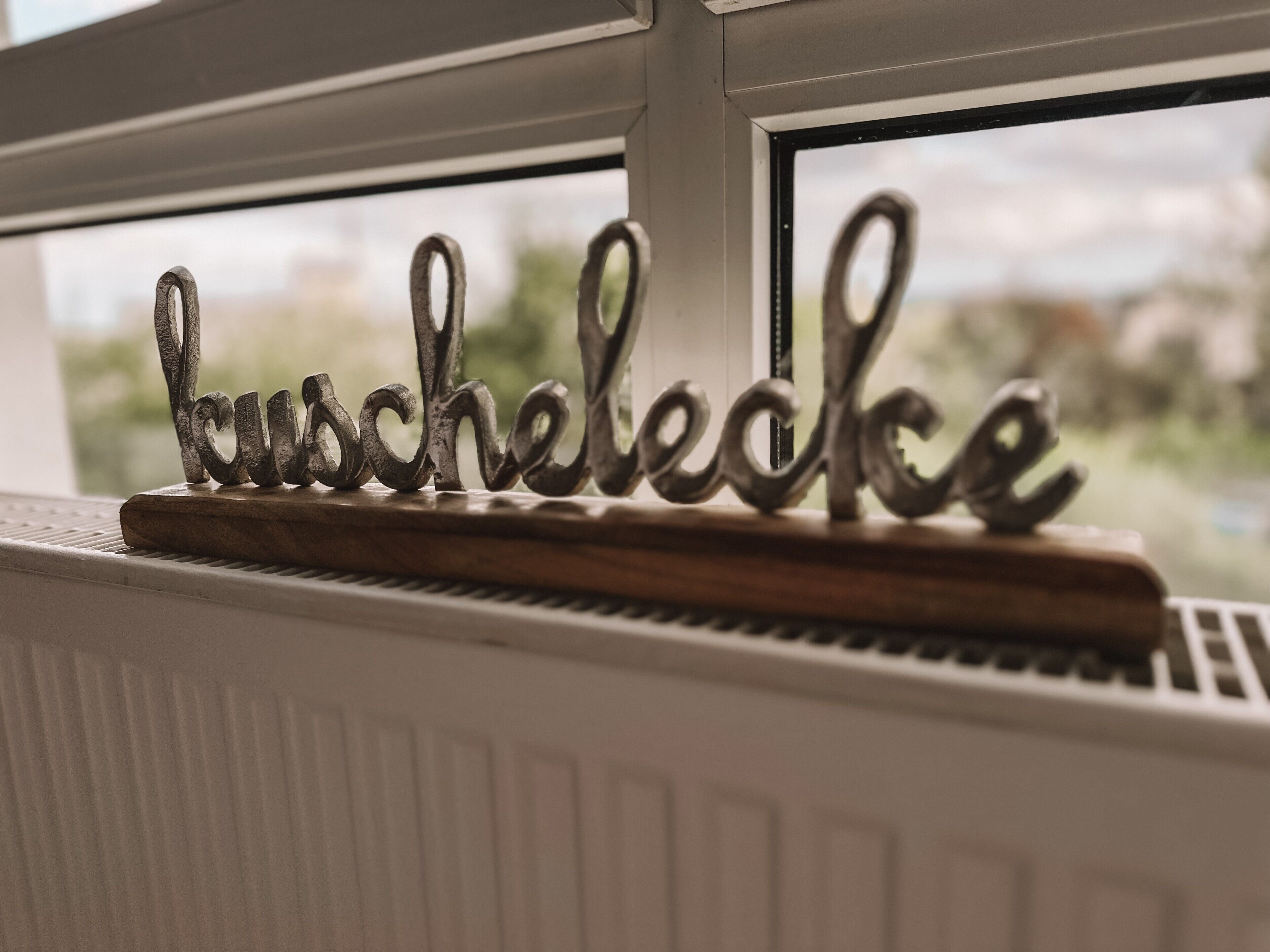 Een metalen bord met de tekst 'Bauschlecke' op een houten voetstuk, geplaatst op een radiator naast een raam.