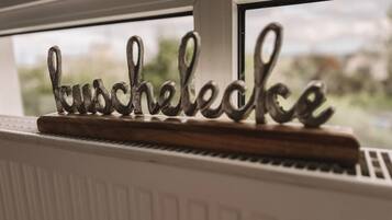 Een metalen bord met de tekst 'Bauschlecke' op een houten voetstuk, geplaatst op een radiator naast een raam.