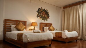 Two wooden beds with white bedding, a wall-mounted lamp, and a large floral artwork. - Kingaling Hotel (Punakha)
