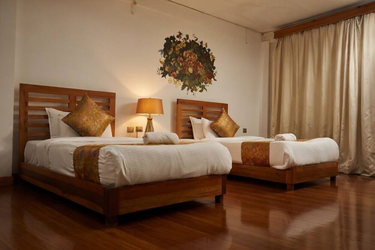 Two wooden beds with white bedding, a wall-mounted lamp, and a large floral artwork.