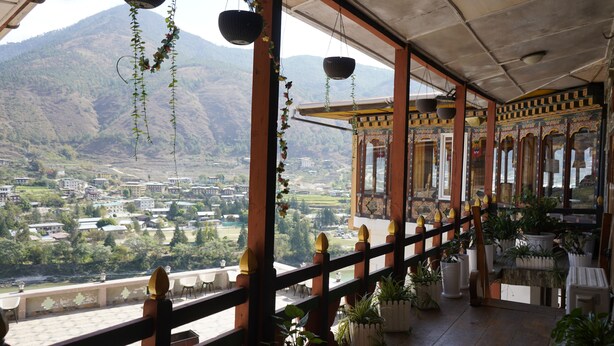 A balcony with a view of a valley and mountains, wooden railings, and potted plants. - Kingaling Hotel (Punakha)