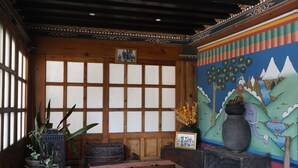 A traditional room with tatami flooring, a low wooden table, a large window with grid patterns, and a colorful mural depicting nature. - Kingaling Hotel (Punakha)
