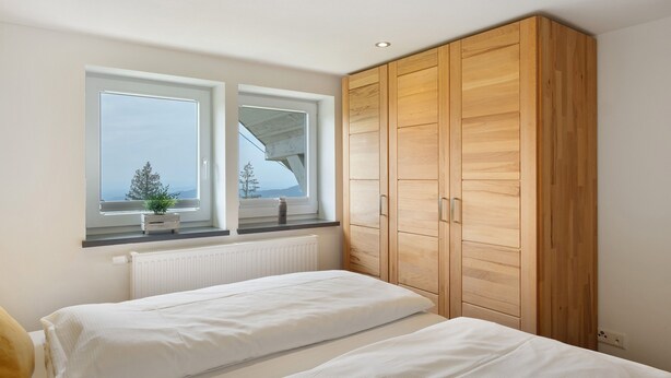 A bedroom with two beds, a wooden wardrobe, a window with a view, and a radiator. - Apartment Zwergenschlössle with Private Garden and Wi-Fi (Breitnau)