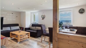 A modern living room with a sofa, a coffee table, and a dining area with a table and chairs. - Apartment Zwergenschlössle with Private Garden and Wi-Fi (Breitnau)