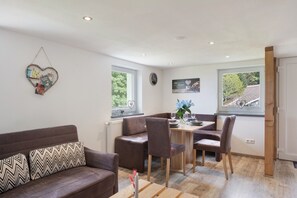 Un salon moderne avec un canapé marron, une table à manger avec des chaises et une fenêtre donnant sur des arbres.