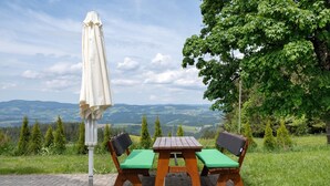 A picnic table with green cushions, a white umbrella, and a view of distant hills. - Apartment Zwergenschlössle with Private Garden and Wi-Fi (Breitnau)