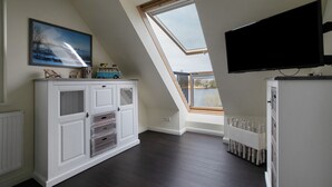 Una stanza con soffitto a falda, un'ampia finestra, una televisione a schermo piatto e un mobile contenitore con cassetti.