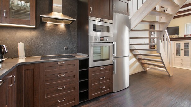 Una cucina moderna con elettrodomestici integrati, una scala in legno e vista sull'area soggiorno.