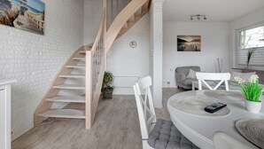 Un intérieur moderne avec un escalier, des murs en briques blanches, un coin repas avec une table ronde et un canapé.