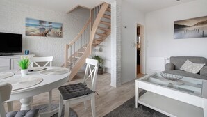 Un salon moderne avec un escalier, des murs blancs et un téléviseur à écran plat.