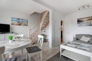 A modern living room with a staircase, white walls, and a flat-screen TV.