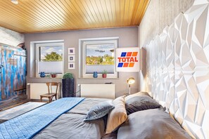 A bedroom with a bed, a chair, a window, a radiator, and a wall-mounted lamp.