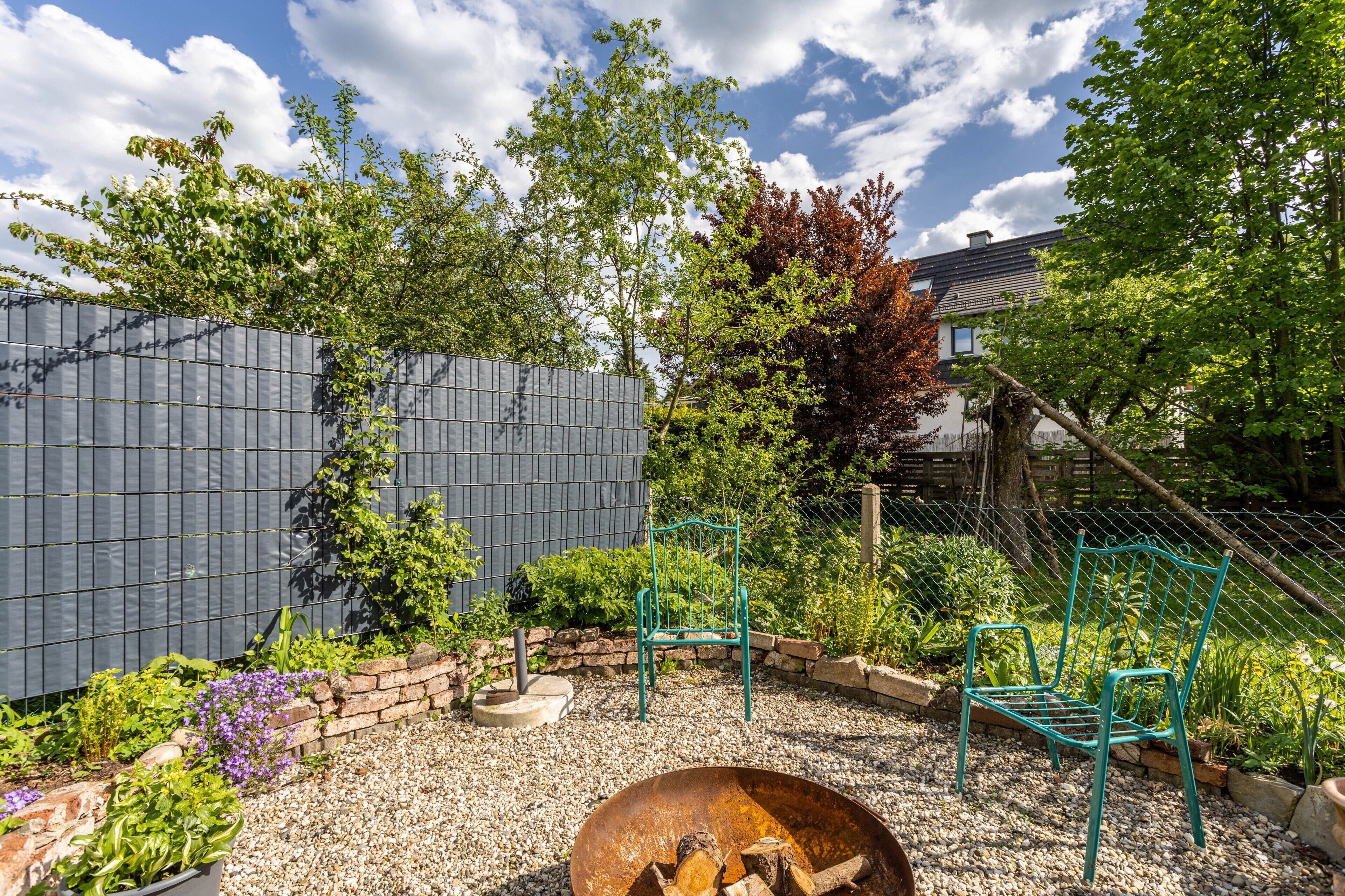 Ein Garten mit einem Metallstuhl, einer Schubkarre und einer Mauer aus Ziegelsteinen.