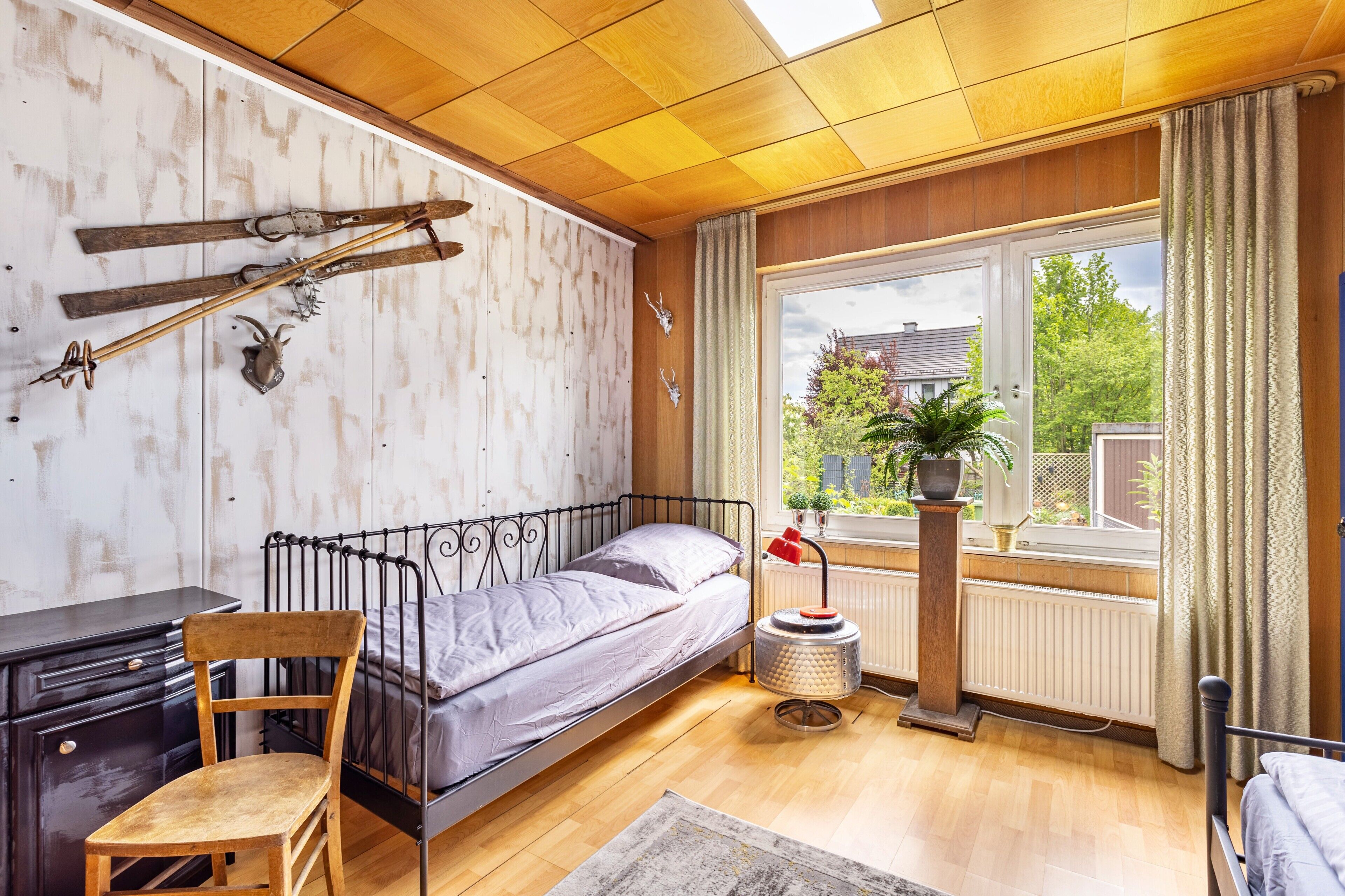 Ein Schlafzimmer mit einem Bett, einem Holzsessel, einem Schreibtisch, Skiern und Geweihen an der Wand.